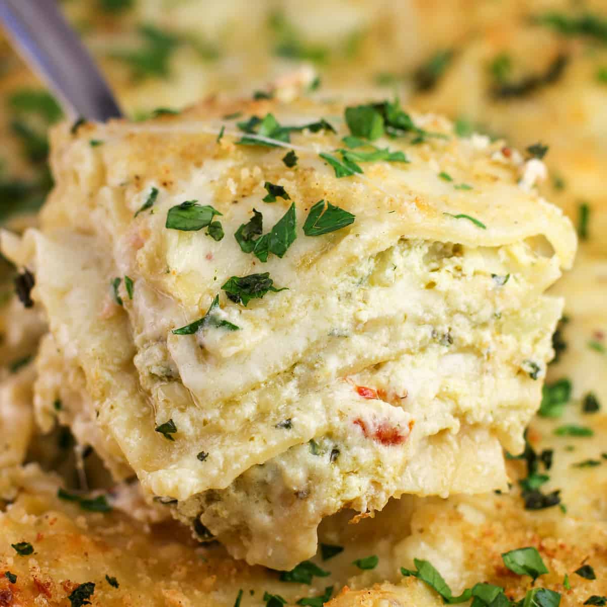 close view of a spatula holding a large square of pesto salmon lasagna to show the layers